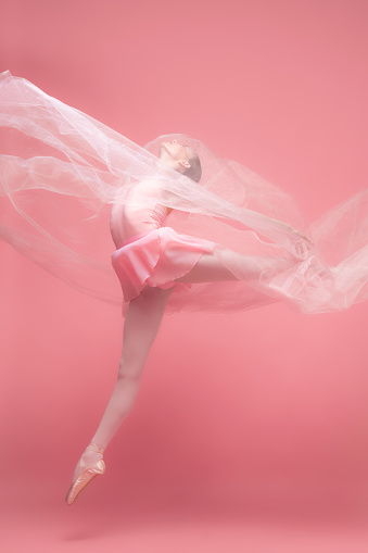 Tenderness and purity. Beautiful girl, graceful female ballet dance dancing with white veiling isolated on pink studio background. Art, motion, action, inspiration concept.. Classiacal ballerina in pointe shoes