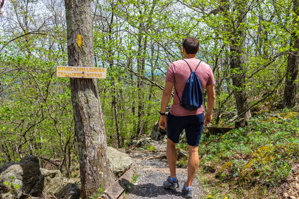 One young man with drawstring bag backpack walking on Wintergreen ski resort village town nature Highlands leisure hiking trail in forest of Virginia in spring with sign One young man with drawstring bag backpack walking on Wintergreen ski resort village town nature Highlands leisure hiking trail in forest of Virginia in spring with sign drawstring backpack stock pictures, royalty-free photos & images