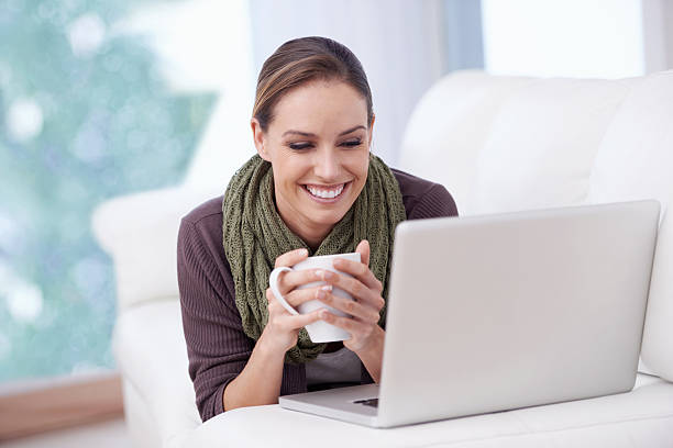 Online coffee break A young woman holding a cup of coffee while lying in front of her laptop in front of stock pictures, royalty-free photos & images