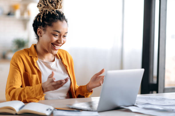Online communication. Confident joyful beautiful african american young female student or freelancer with afro dreadlocks, study remotely, talks by online conference with coworkers or teacher, smile stock photo
