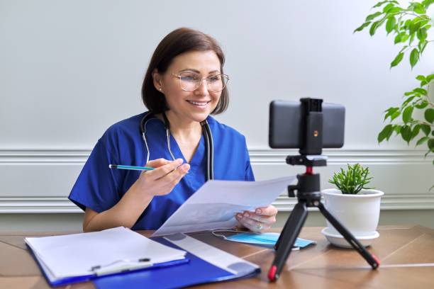 Online doctor consultation, female talking with patient using video call Online doctor consultation, female specialist talking with patient using video call, smartphone on tripod, doctor with stethoscope looking at the phone's webcam nurse talking to camera stock pictures, royalty-free photos & images