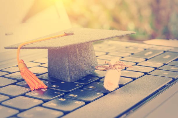 online learning or e-learning and online graduate certificate program concept : Black graduation cap, diploma on a laptop computer keyboard, depicts distant learning can be done via cyber / internet  MBA stock pictures, royalty-free photos & images