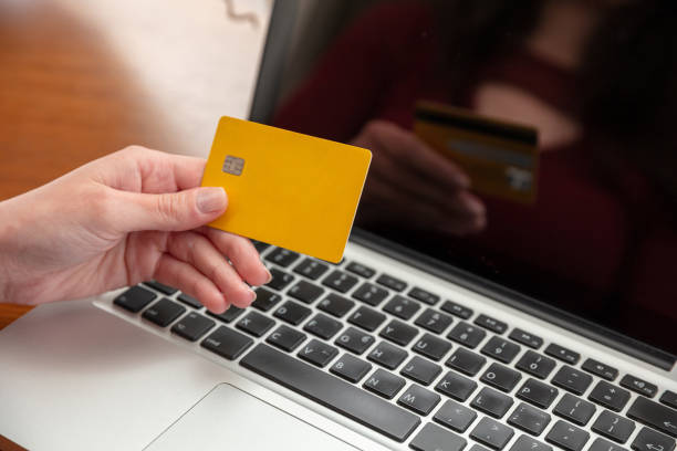 Online shopping. Credit card in hand and computer laptop, wooden table, close up view. stock photo