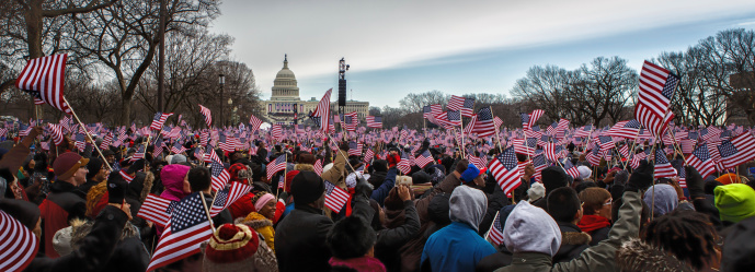 Washington, USA - January 21, 2012: Onlookers holding American flags on the National Mall observe Inauguration of Barack Obama as the President in Washington, DC on January 21, 2013. Barack Obama is the 44th president of USA and the first African American to hold presidential office in the United States.