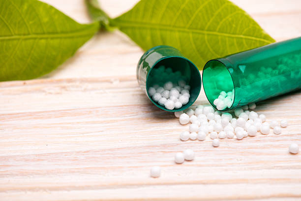 Open capsule with small white balls and green leaf Open capsule with small white balls and green leaf on wooden table homeopathic medicine stock pictures, royalty-free photos & images