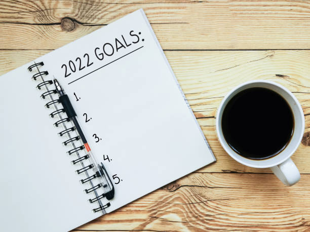 Open notebook with text "2022 Goals" and a cup  of coffee on wooden background. stock photo