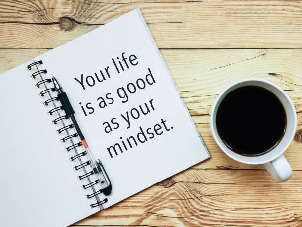 Open notebook with text "Your life is as good as your mindset" and a cup  of coffee on wooden background. stock photo
