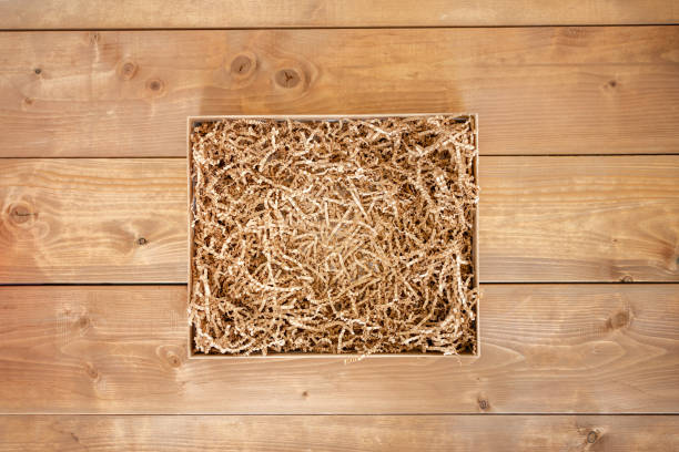 Opened gift box with shredded paper on wooden background. Flat lay, top view. Box for your product replacement. stock photo
