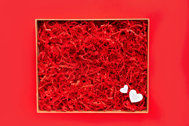 Opened gift box with shredded red paper on plain red background. Flat lay, top view. Box for your product replacement. Valentine's stock photo