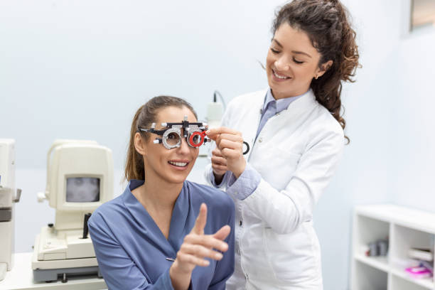 Optometrists changes lenses in trial frame to examine the vision of young woman patient vision at ophthalmology clinic, selective focus stock photo