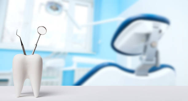 Oral dental hygiene. Healthy white tooth and dentist mirror with explorer probe instrument against blurred dentist Office background with dental chair and lamp. Oral dental hygiene. Healthy white tooth and dentist mirror with explorer probe instrument against blurred dentist Office background with dental chair and lamp dentists office stock pictures, royalty-free photos & images