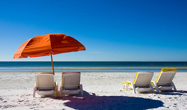 Orange beach umbrella and empty lounge chairs facing the sea stock photo