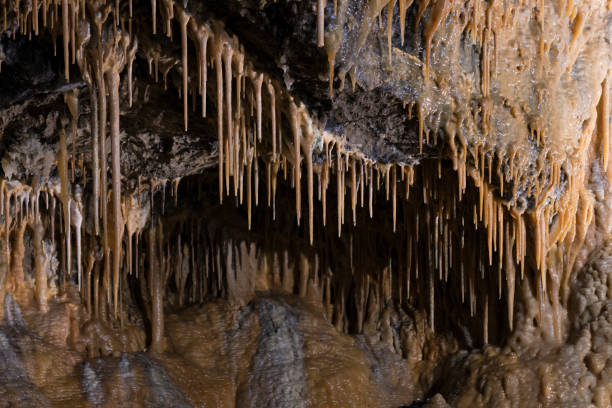 Orange Calcite Stalactites Orange calcite stalactites hanging down from a cave's ceiling in Derbyshire, UK. peak district national park stock pictures, royalty-free photos & images
