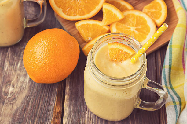 Orange fruit smoothie in the glass jar Orange fruit smoothie in the glass jar with fresh orange slices on rustic wooden background orange smoothie stock pictures, royalty-free photos & images