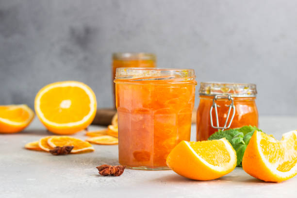 Orange jam or marmalade in glass jar, fresh and dried orange fruit slices, mint and spices on light grey background. Orange jam or marmalade in glass jar, fresh and dried orange fruit slices, mint and spices on light grey background. marmalade stock pictures, royalty-free photos & images