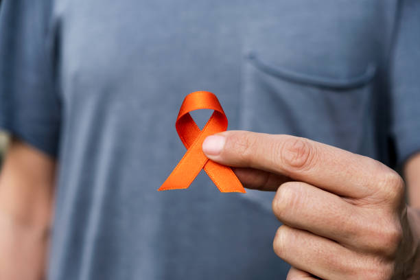 orange ribbon in support of multiple sclerosis closeup of a young caucasian man with an orange ribbon in his hand, in support of people affected by multiple sclerosis multiple sclerosis stock pictures, royalty-free photos & images
