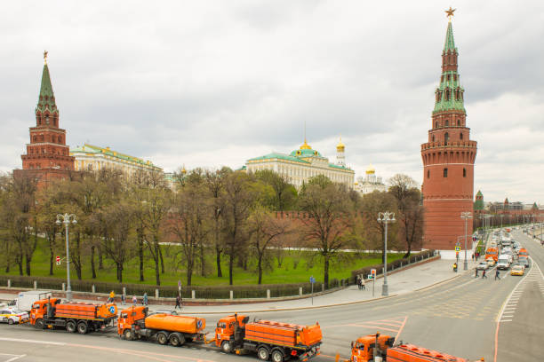 orange road-washing water trucks in the city in front of the red brick wall and the Kremlin towers A row of orange road-washing water trucks in the city in front of the red brick wall and the Kremlin towers among green trees on a cloudy day. Concept - work of municipal in Moscow public service stock pictures, royalty-free photos & images