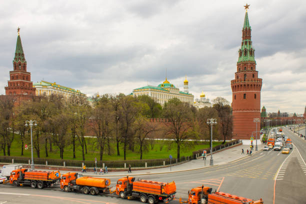 orange road-washing water trucks in the city in front of the red brick wall and the Kremlin towers A row of orange road-washing water trucks in the city in front of the red brick wall and the Kremlin towers among green trees on a cloudy day. Concept - work of municipal in Moscow public service stock pictures, royalty-free photos & images