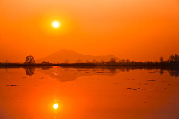 Orange sun over serene lake with reflection stock photo