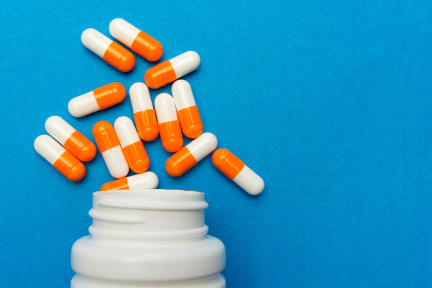 Orange white capsules (pills) were poured from a white bottle on a blue background. Medical background, template. stock photo
