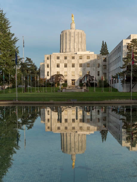 Oregon State Capitol Building with Reflection Flags Blue Sky A side view of the Oregon State Capitol building from across a water feature with capitol reflection. Located at the State Capital Salem, Oregon. Edited in Photoshop. oregon state capitol stock pictures, royalty-free photos & images