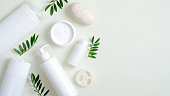 Organic herbal cosmetic products on green background. Top view beauty spa cosmetic bottle packaging, hand cream, lotion, bath sponge, natural soap and green leaves. Minimalist beauty product mockups