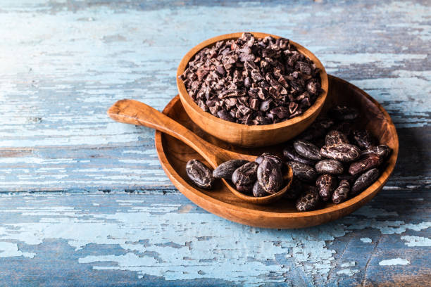Organic raw cocoa beans, nibs in wooden bowls on blue rustic background. stock photo