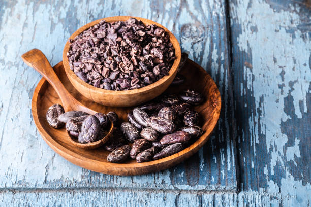 Organic raw cocoa beans, nibs in wooden bowls on blue rustic background with copyspace close-up stock photo