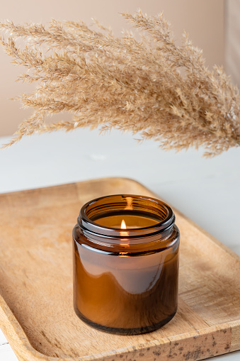 Organic scented soy candle in dark glass jar on the bamboo tray. minimalism concept. Close up, copy space for text Zero waste minimalism concept, handmade candle with dry reed grass.