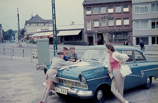Lower Saxony (unfortunately the exact location is not known), Northern Germany, 1963. Break during a weekend trip by car. Family searches for the best road connection to their destination using a map spread out on the bonnet. Also: locals, shops and buildings.