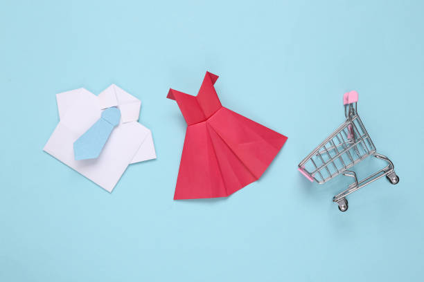 Origami hand made paper red dress and shirt with tie, shopping trolley on blue background. Shopping concept stock photo