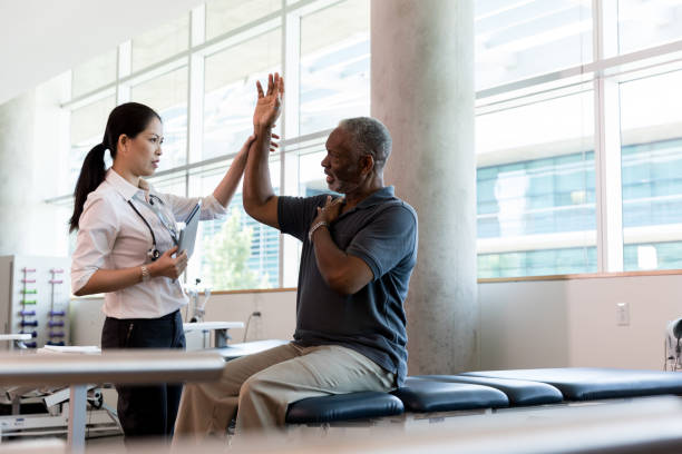 Orthopedic doctor checks patient's range of motion Confident female orthopedic doctor has a senior male patient lift his hand over his shoulder, testing his range of motion in his arm. physical therapy stock pictures, royalty-free photos & images