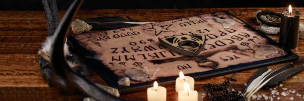 Ouija Board with candles. Seance on wooden table. The mystical atmosphere of the call of spirits. Black magic. Ouija Board with candles. Seance on wooden table. The mystical atmosphere of the call of spirits. Black magic. Close-up. ouija board stock pictures, royalty-free photos & images