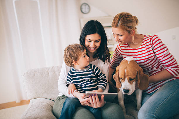 Our cute family Photo of family, two women, dog and cute little boy, are sitting on the sofa in their living room and using tablet child lover stock pictures, royalty-free photos & images