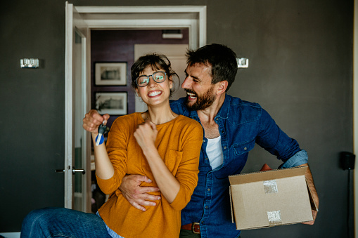 Portrait of a happy woman and a man, holding keys from the new first house, a young family of two celebrating moving day, satisfied customers couple purchase real estate, mortgage, and relocation concept