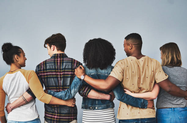 Our friends become our family Rearview studio shot of a diverse group of young people embracing each other against a gray background arm around stock pictures, royalty-free photos & images