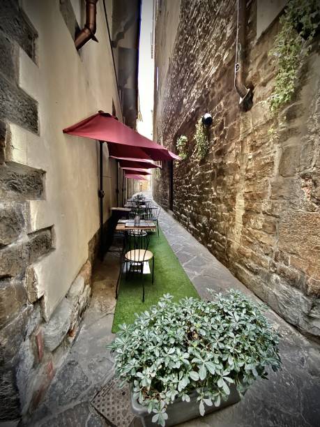 outdoor dining tables all in a row, diminishing down a narrow stone walkway in florence, tuscany, italy. stock photo