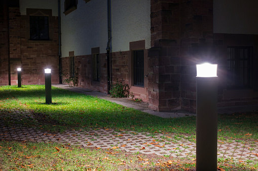 Outdoor lights (lanterns, bollards) in front of an old administration building illuminating a walkway in the garden at night