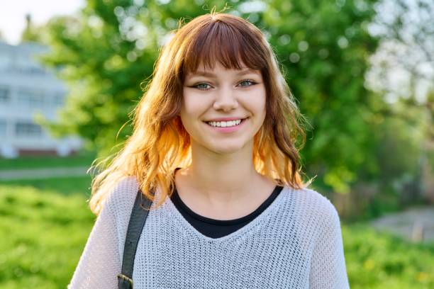 Outdoor portrait of beautiful smiling teen female student with backpack looking at camera stock photo