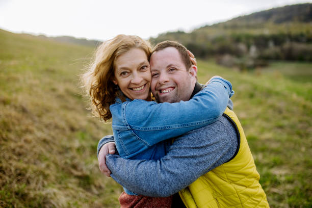 Outdoor portrait of mother hugging her grown up son with Down syndrome, motherhood concept. stock photo