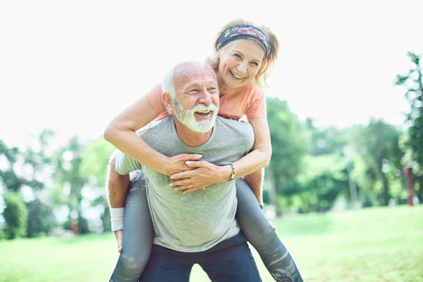 outdoor senior fitness woman man lifestyle active sport exercise healthy fit retirement love fun piggyback stock photo