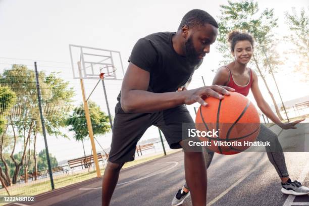 Outdoors Activity. African couple guy dribbling concentrated while girl defencing backdoor playful on basketball court close-up