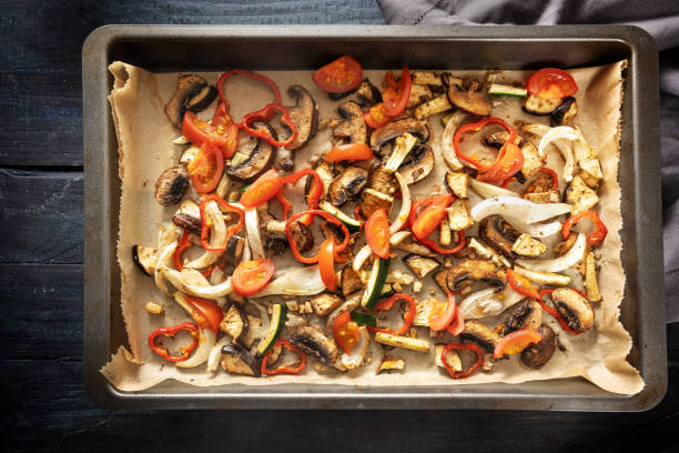 Oven vegetables like bell pepper, tomato, zucchini, mushroom, fennel and eggplant on a baking tray on dark rustic wood, high angle view from above stock photo