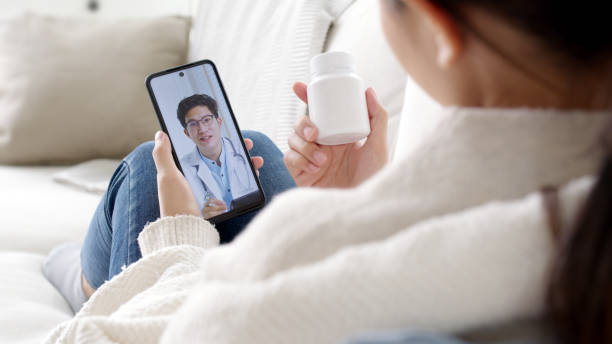 Over shoulder view of young asia woman talk to doctor on cellphone videocall conference medical app in telehealth telemedicine online service hospital quarantine social distance at home concept. stock photo