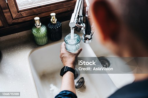istock Over the shoulder view of senior Asian man filling a glass of filtered water right from the tap in the kitchen at home 1368715188
