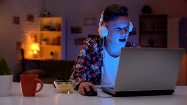 l’adolescence overémotionnelle jouant le jeu d’ordinateur sur l’ordinateur portatif et mangeant des collations, addiction - parent adolescent anxiété photos et images de collection
