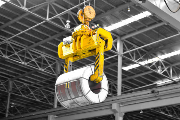 Overhead crane lift up steel coil with tong in warehouse. Steel coils handling equipment. Steel warehouse and logistics operations. Overhead crane lift up steel coil with tong in warehouse. Steel coils handling equipment. Steel warehouse and logistics operations. steel mill stock pictures, royalty-free photos & images
