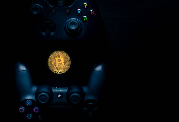 Overhead shot of a Playstation and Xbox controller next to a physical Bitcoin. SHEFFIELD, UK - JUNE 2ND 2019: Overhead shot of a Microsoft black Xbox one controller and A Sony black Playstation 4 controller with a physical gold bitcoin in the middle of them both against a black background xbox stock pictures, royalty-free photos & images