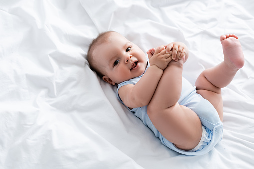 overhead view of baby boy touching legs while lying on bed