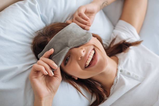 overhead view of happy young woman in eye mask resting in bedroom overhead view of happy young woman in eye mask resting in bedroom eye mask stock pictures, royalty-free photos & images